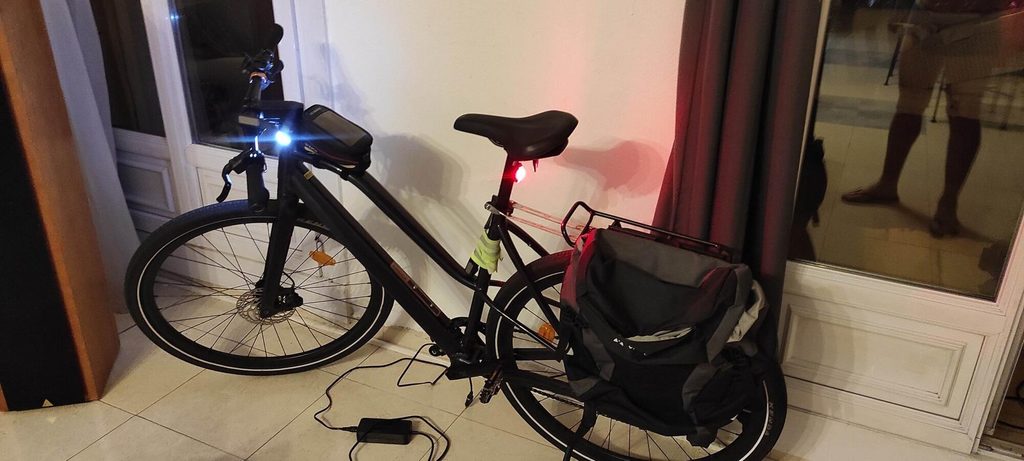 Commuter bicycle with front and rear lights, helmet, and charging accessories arranged in a compact home cycling area.
