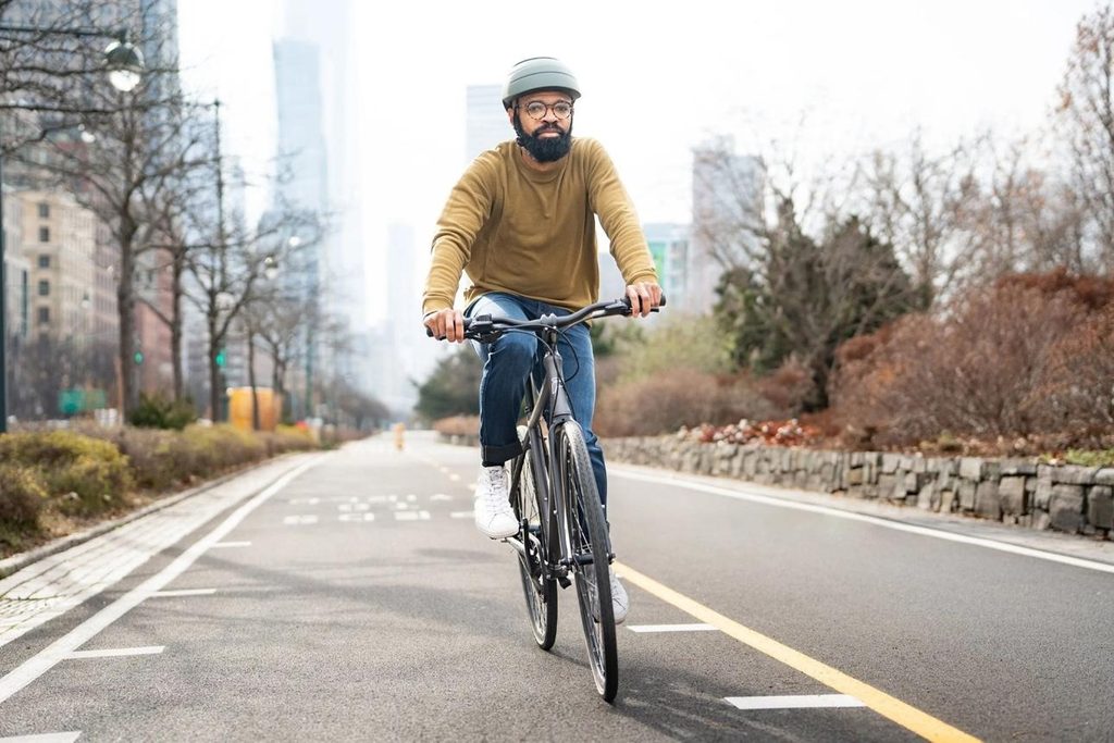 Casual cyclist wearing a properly fitted bicycle helmet on a paved bike path.